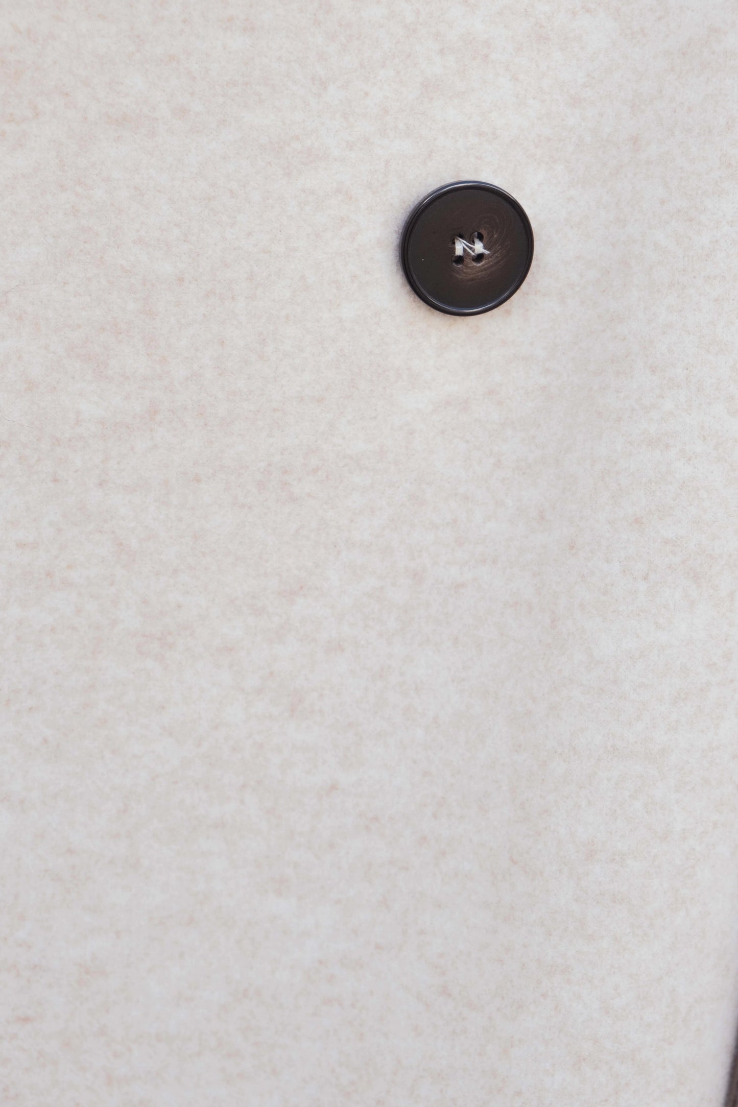 Macro del botón contrastado sobre tejido beige del abrigo cruzado, acabado pulido – Zenda Couture
