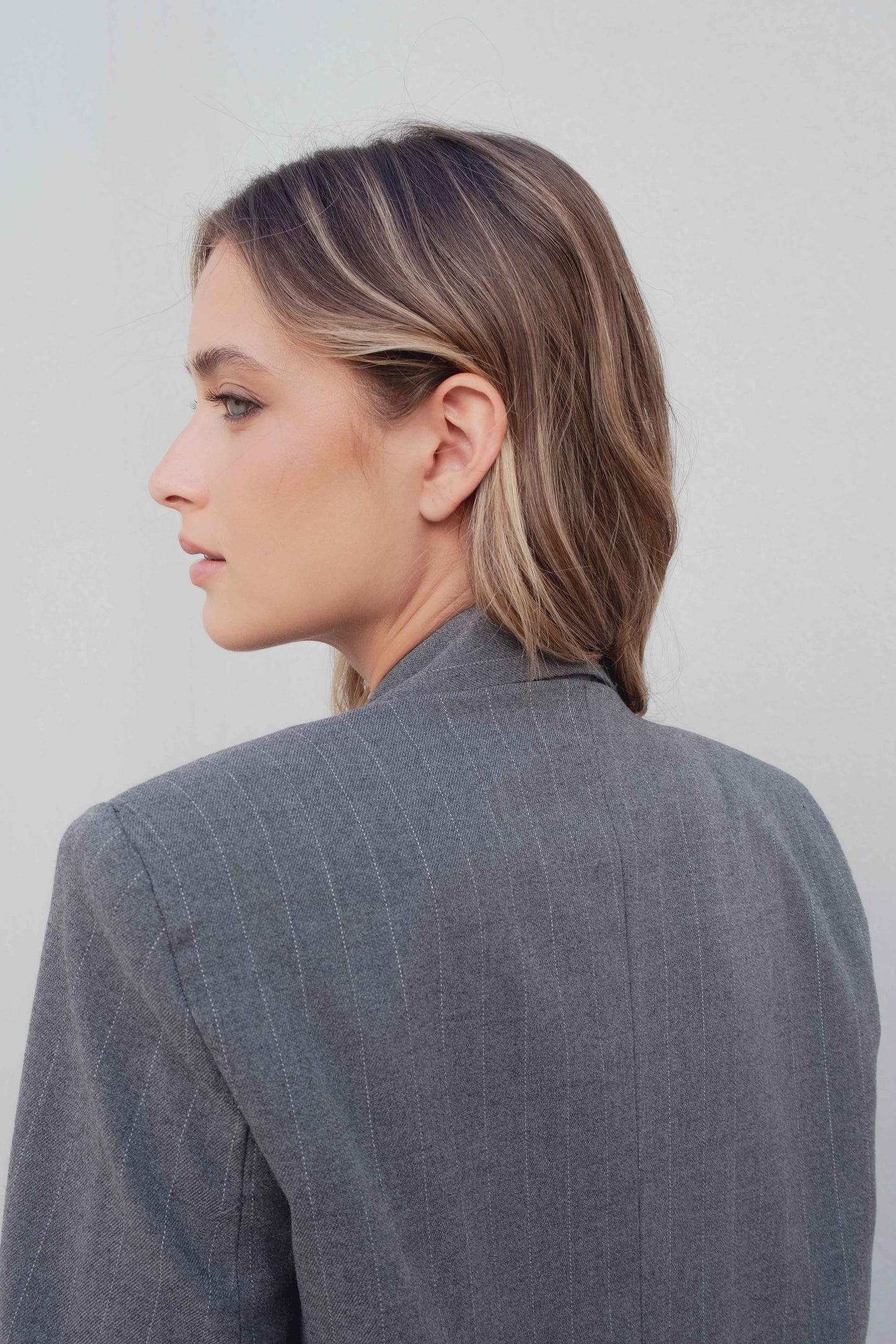 Vista trasera del blazer raya diplomática gris con hombro estructurado y caída limpia – Zenda Couture