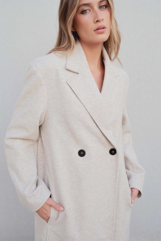 Detalle de solapa de muesca y cierre cruzado con dos botones en abrigo beige de acabado suave – Zenda Couture