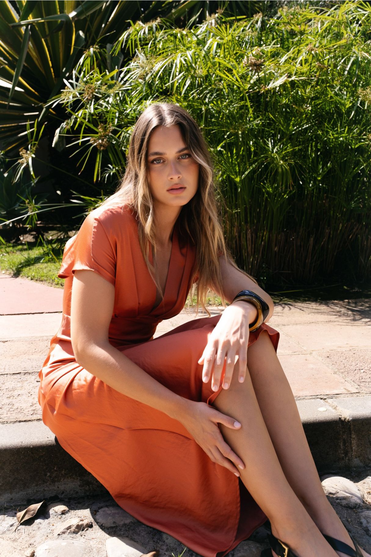 Modelo con vestido midi satinado en color teja, posando al aire libre